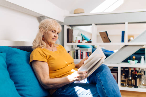 istock Mature woman reading a book on the sofa 1280028752