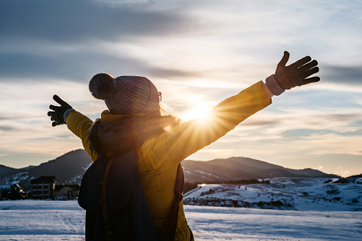 Young happy smiling woman with open arms in a winter sunset on mountain.