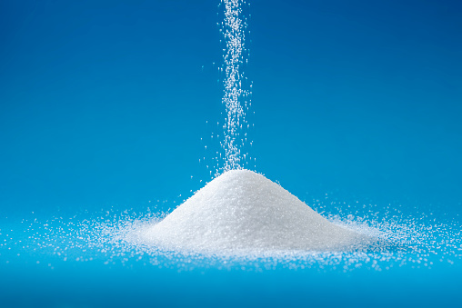 Heap of sugar with pouring sugar on blue background,