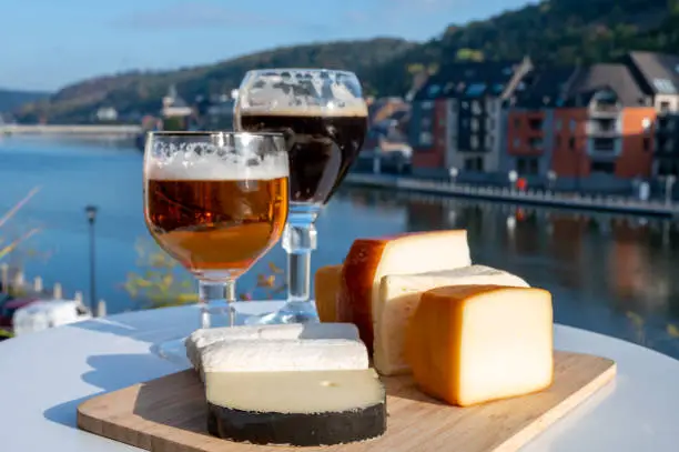 Glass of strong Belgian abbey beer and tasting of cheeses made with trappist beer and fine herbs with view on Maas river in Dinant, Wallonia, Belgium
