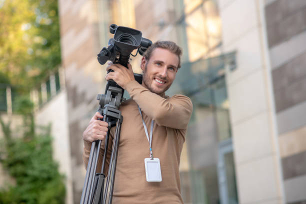 istock Delighted fair-haired cameraman carring camera with tripod outside 1280043509