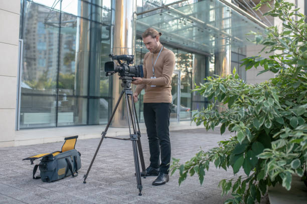 Busy cameraman fixing camera to tripod in front of modern building