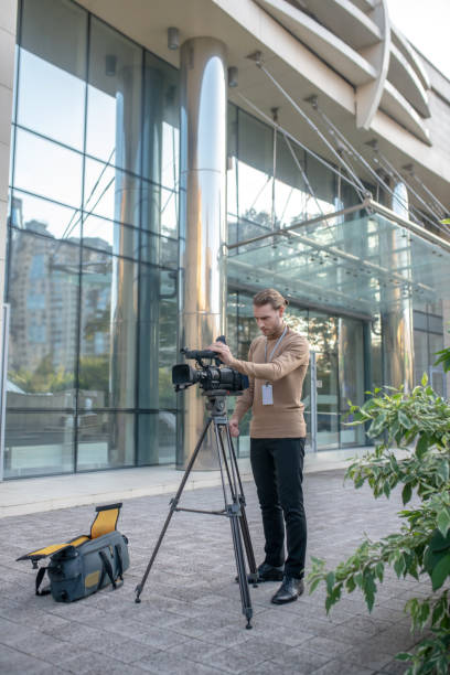 istock Fair-haired cameraman fixing camera to tripod in front of modern building 1280044172