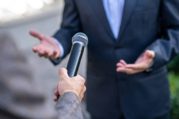 istock Close-up of male hands holding microphone during interview 1280044293