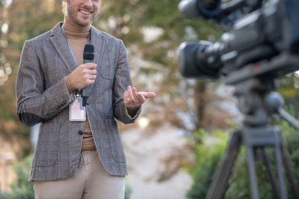 istock Male reporter speaking into microphone in front of camera outside 1280044366