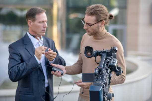 istock Fair-haired operator helping male reporter fit headset 1280044375