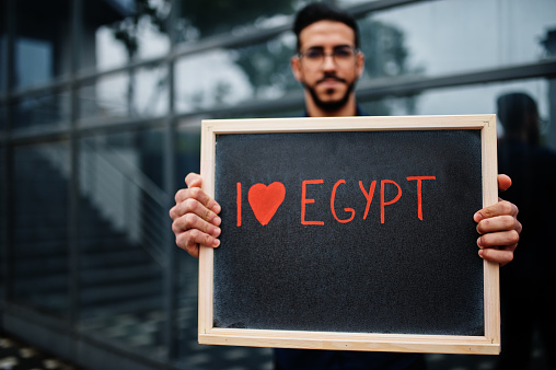 I love Egypt. Middle eastern man wear blue shirt, eyeglasses, hold board.