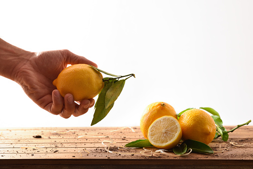 Hand with harvest lemon in hand and lemons on wooden table on white isolated background. Front view. Horizontal composition.