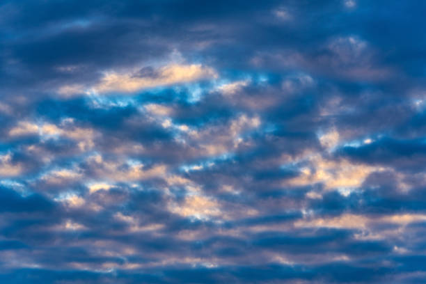 Dramatic clouds in blue sky, illuminated by rays of sun at sunset to change summer weather. Soft focus, motion blur multicolored cloudscape background.