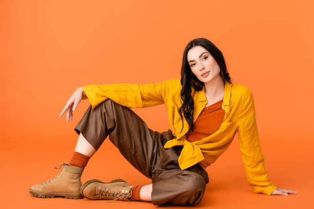 fashionable young woman in autumn outfit and boots looking at camera while sitting on orange - women beautiful studio shot full length imagens e fotografias de stock