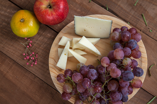 Top view of cheese plate with grapes, tangerine and red apple, on wooden table