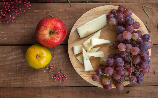 Top view of cheese plate with grapes, tangerine and red apple, on wooden table