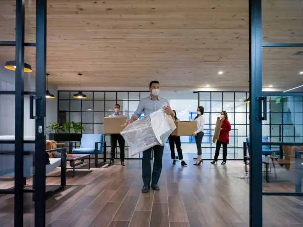 Group of business people moving into a new office wearing facemasks during the COVID-19 pandemic - reopening of businesses