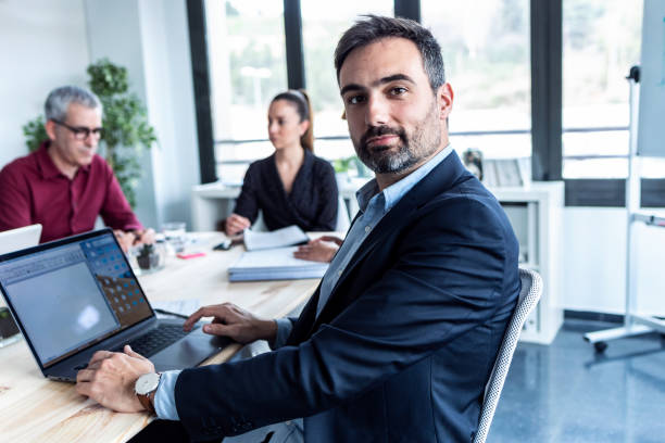 istock Handsome businessman is looking at camera while his colleagues are working on coworking place. 1280056389