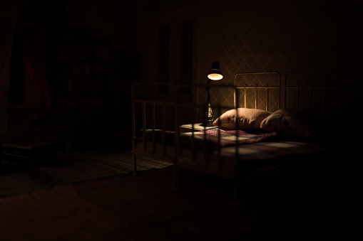 Old vintage single bed at night . A realistic dollhouse bedroom with furniture and window. Selective focus