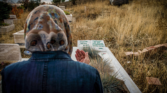 Muslim woman praying by the tombstone in cemetery. Depth of field done intentionally.