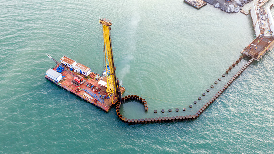 Aerial view of the piles of the under construction new pier and A pile driver. Pile driver is a device used to drive piles into soil to provide foundation support for buildings or other structures.