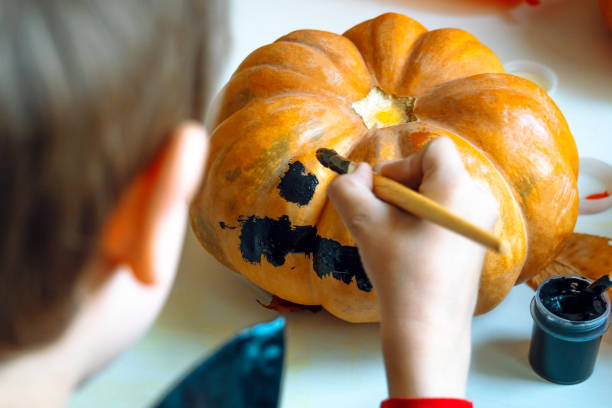 istock Little boy paints the pumpkin by black paint. Close up. 1280058385