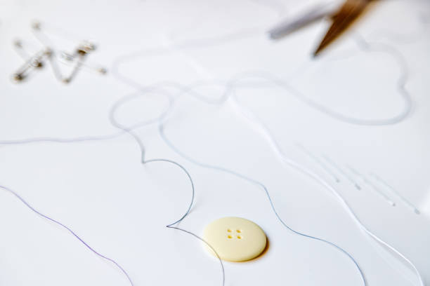 istock Macro close-up of a button next to colored threads, scissors, threader, needles, and safety pins, against white background 1280060722