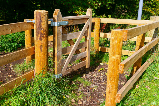 A rural countryside kissing gate, made from wood and designed to let people through when walking across agricultural land, while keeping livestock safe. The metal hinged gate is pushed to allow ramblers through and closes itself without the need for latches.