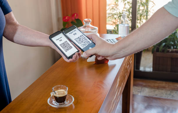 Hands of two adults holding smartphones and using dynamic QR Code for payment at the coffee shop with new Instant Payment mode - “PIX” stock photo