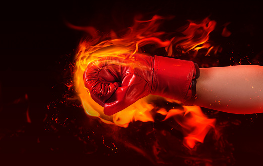 Photo of male hand in red boxing glove punching fire on burning background.