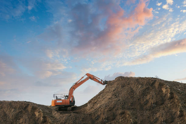 An excavator digging up dirt in a sand pit Excavator bulldozer in sandpit with raised bucket over blue cloudscape sky. quarry stock pictures, royalty-free photos & images