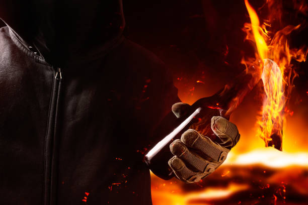 Protestant in mask and hood holding burning molotov cocktail. stock photo
