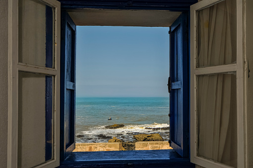 An old wooden blue window with the view of the beach in the background