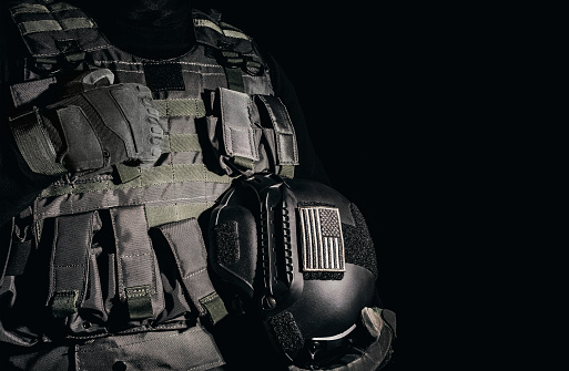 Soldado con guantes tácticos y chaleco de armadura de pie y sosteniendo casco militar. photo