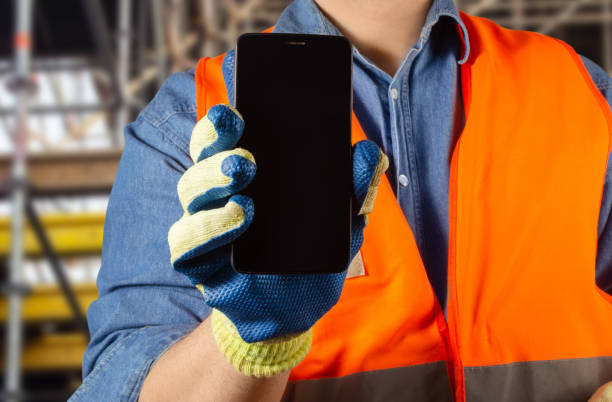 istock Worker in orange jacket uniform and gloves holding a black smartphone. 1280072568
