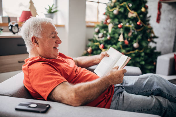 istock Senior man reading a book by the Christmas tree at home 1280077340