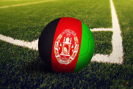 Afghanistan flag on ball at corner kick position, soccer field background. National football theme on green grass.