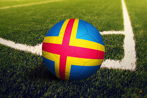 Aland Islands flag on ball at corner kick position, soccer field background. National football theme on green grass.