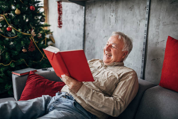 istock One cheerful senior man sitting on the sofa and reading a book 1280079607