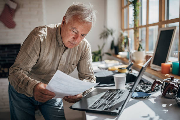 istock Senior man standing in the kitchen and working on the laptop 1280080537