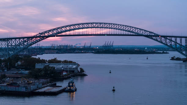 Tugboats are moored in front of the Bayonne Bridge connecting New Jersey, and New York State at sunset, with the remote view of the commercial docs and a port in the backdrop. Aerial scenic views of the Bayonne Bridge connecting New Jersey, and New York State at sunset. bayonne stock pictures, royalty-free photos & images