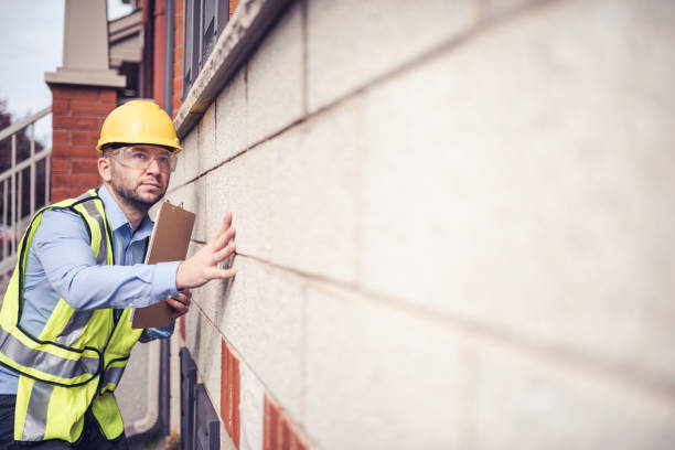 Building inspector at work Building inspector, architect, engineer, general contractor, repairman insurance adjuster, or other blue collar worker inspecting a residential building. Wearing a safety vest, yellow helmet and clear safety glasses, he is checking very meticulously every deficiency and takes notes on the clipboard inspector stock pictures, royalty-free photos & images