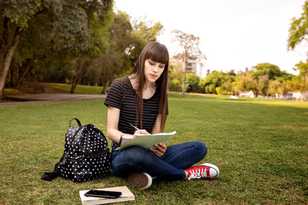 istock Young woman studying on campus grass 1280086973