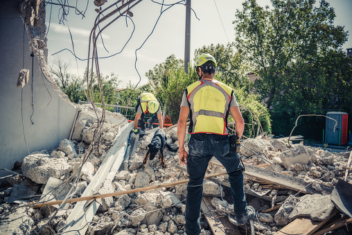 Rescuer search trough ruins of building with help of rescue dog.