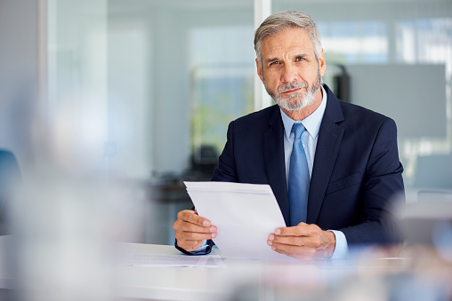 Portrait of confident mature businessman holding documents while sitting in office