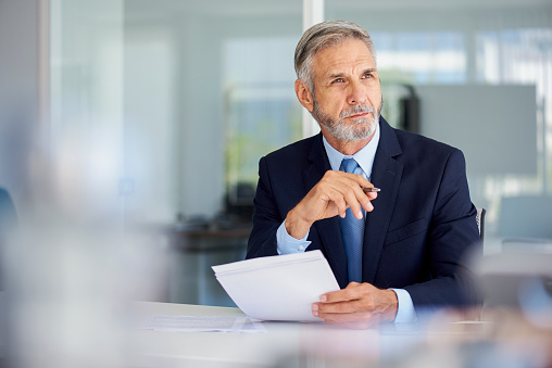 Portrait of thoughtful mature businessman holding documents while sitting in office