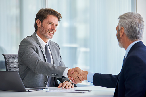 Two smiling mature businessmen shaking hands in office