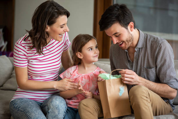 parents donnant le cadeau à la fille à la maison - women holding shopping bag living room photos et images de collection