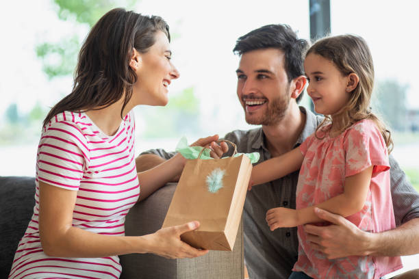 parents donnant le cadeau à la fille à la maison - women holding shopping bag living room photos et images de collection