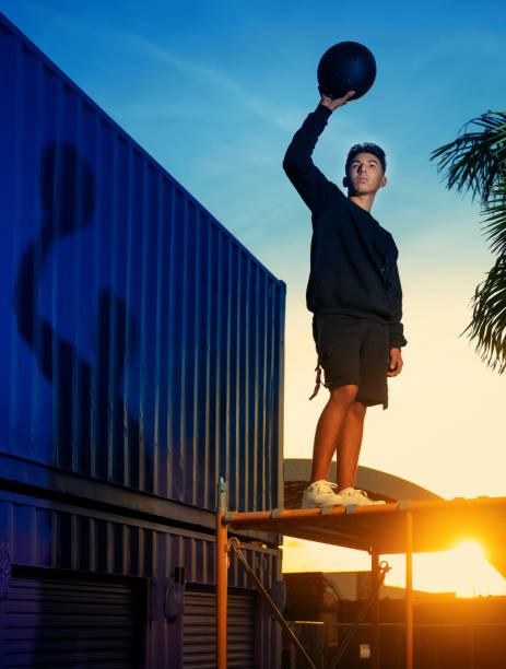 adolescente hispano en la parte superior de un andamio sosteniendo una pelota de baloncesto - miami basketball fotografías e imágenes de stock