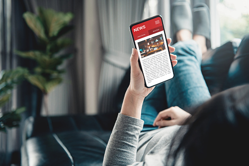 Online news on a smartphone. (Mockup website). Woman reading news or articles in a mobile phone screen application at home. Newspaper and portal on internet, copy space.