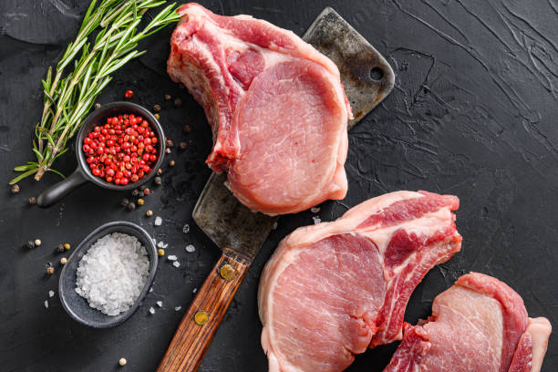 istock Pork chop on a bone in a black round plate on a grey textured  stone background with black cloth  rosemary garlic peppercorns ingredients top view spce for text 1280106927
