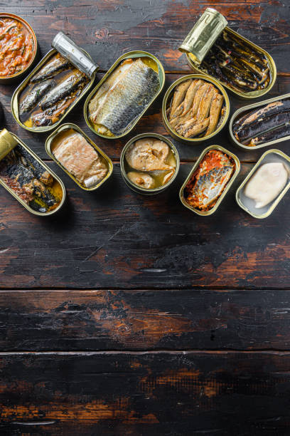 istock opened cans conserve with  Saury, mackerel, sprats, sardines, pilchard, squid, tuna over wood table top view vertical space for text 1280110069
