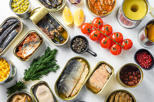 Different canned conserve products in tin cans. with fresh organic ingridients Saury, mackerel, sprats, sardines, pilchard, squid, tuna pinapple, corn, peas, mango ,  beans,   over white textured background top view